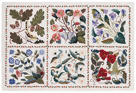 A white wool hand-hooked rug with a floral pattern featuring various colors such as red, blue, and green, and adorned with a bird and butterfly motif.