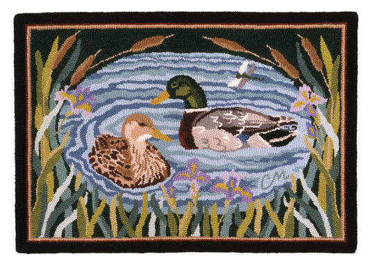 A rectangular hand-hooked rug featuring two mallard ducks swimming in a blue pond, surrounded by reeds and flowers, with a black border.