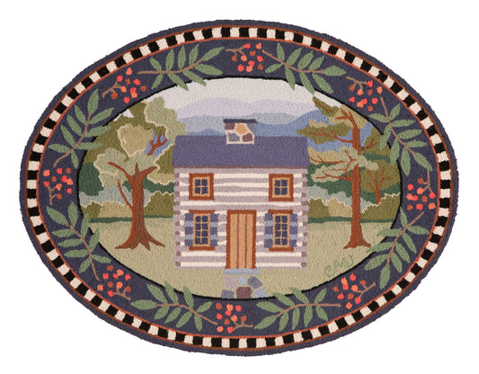 An oval hand-hooked rug featuring a central log cabin scene surrounded by a decorative border of leaves, berries, and geometric patterns.