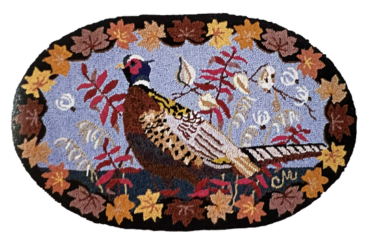 An oval hand-hooked rug featuring a pheasant bird in the center, surrounded by autumn leaves and branches on a light blue background, with a black border.