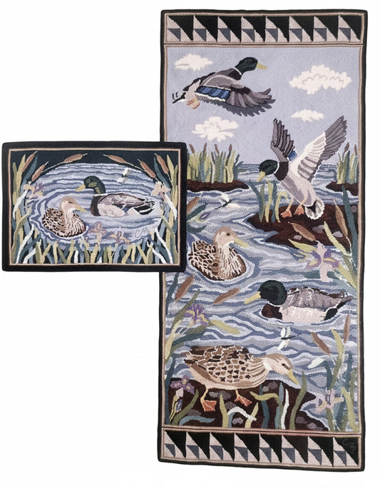 A hand-hooked rug featuring a detailed nature scene of mallards in a marsh, in a blue background with  ducks in brown, black, white, and green, and is framed by a black and white geometric border.